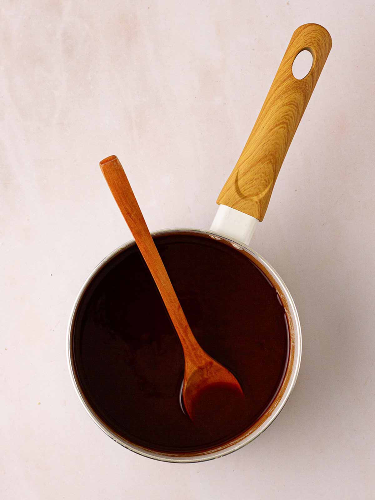 A pan with Peking sauce with a wooden spoon for step 4 in the recipe for Slow Cooker Peking Duck.