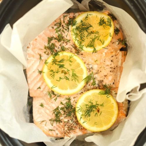 Salmon inside a slow cooker with lemon on dill on top.