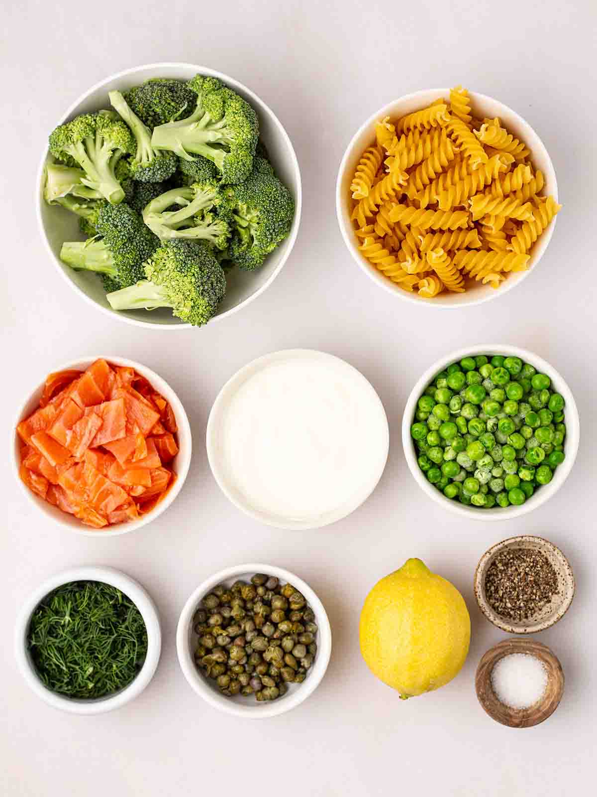The ingredients for smoked salmon pasta in bowls on a white counter.