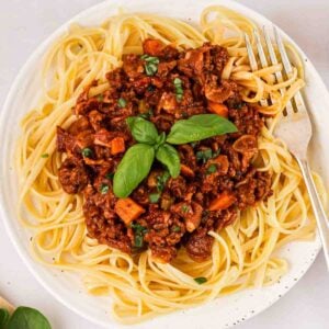 A plate of spaghetti bolognese with a fork in and basil on top.