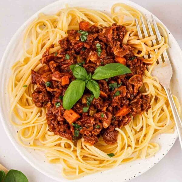 A plate of spaghetti bolognese with a fork in and basil on top.