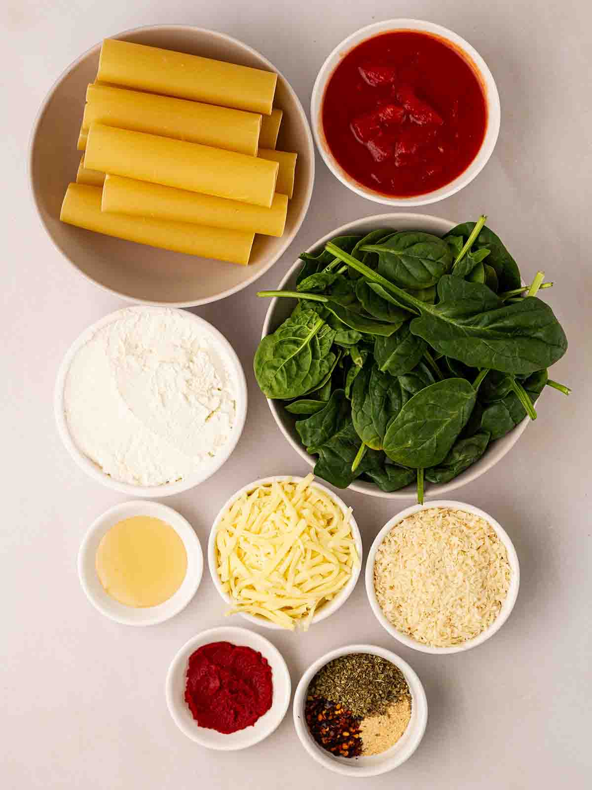 The ingredients for making Spinach and Ricotta Cannelloni laid out in bowls on a white counter.