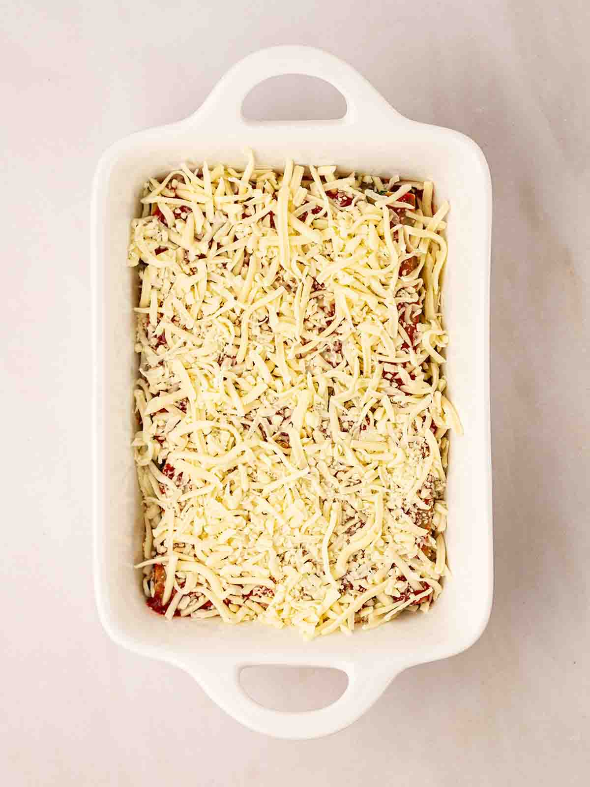 An oven dish filled with uncooked spinach and cannelloni for step 8 in the recipe.