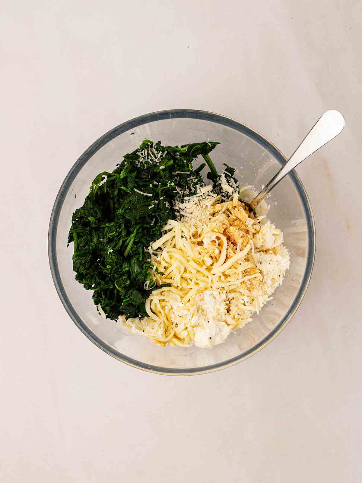 A glass bowl filled with cheese and spinach for step 3 in the recipe for Spinach and Ricotta Cannelloni.