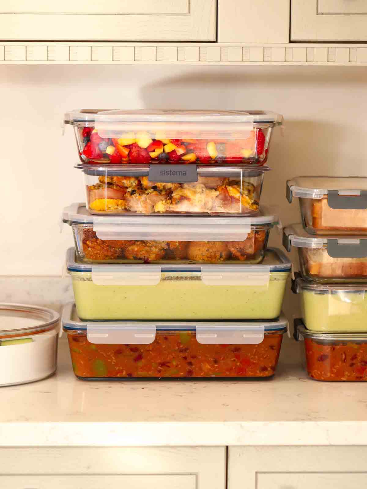 Pile of filled meal prep containers on a kitchen work surface.