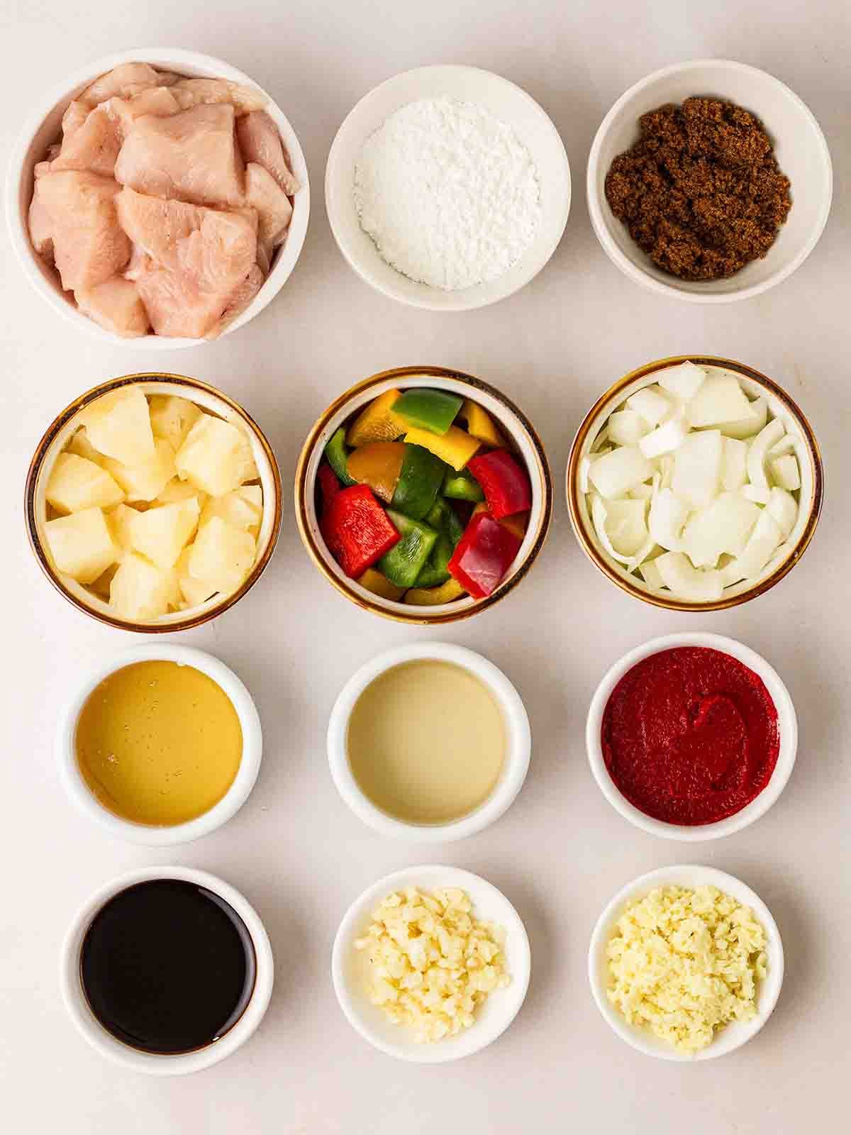 Small bowls of ingredients to make Sweet and Sour Chicken laid out on a white counter.