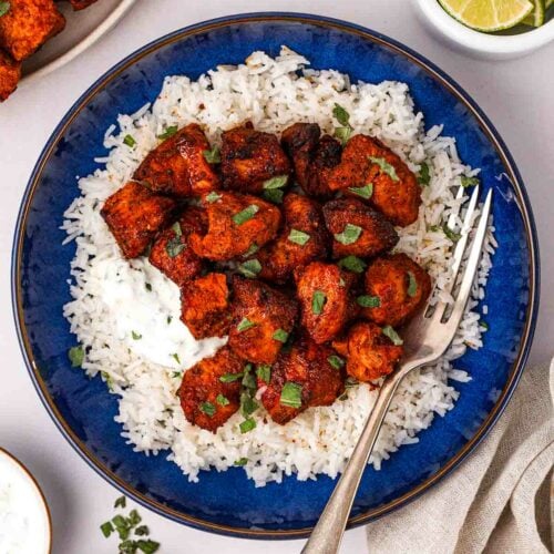 Cooked tandoori chicken and rice on a blue plate with a fork, surrounded by smaller pots.