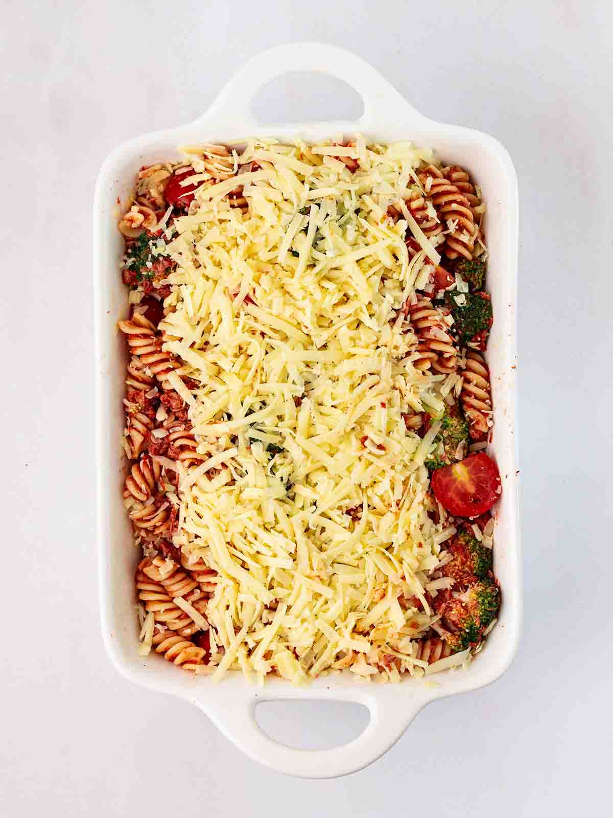 An oven dish filled with tuna pasta mixture and topped with cheese, ready to be baked in the oven.