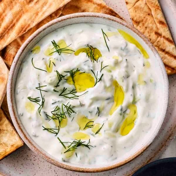 A bowl of easy homemade tzatziki with pittas around the edge.