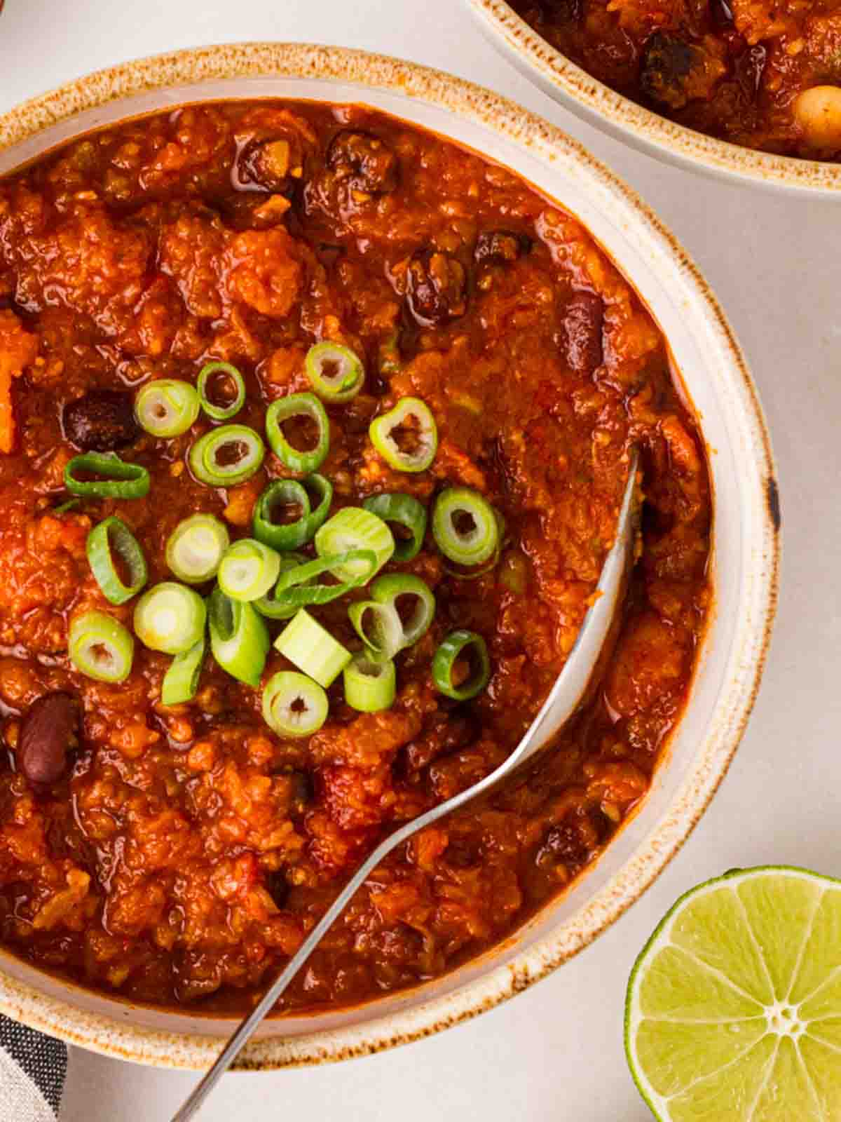 A bowl of vegan chilli with spring onions on top and a spoon to serve.