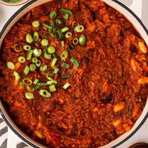A large pot of vegan chilli on a table with spring onions on top.