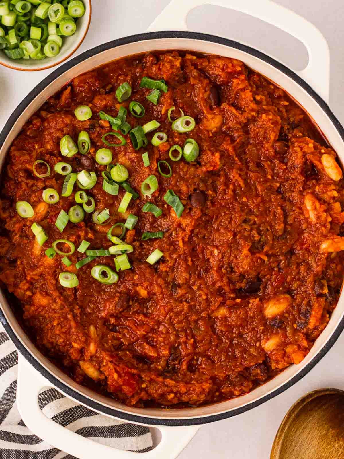 A large pot of vegan chilli on a table with spring onions on top.