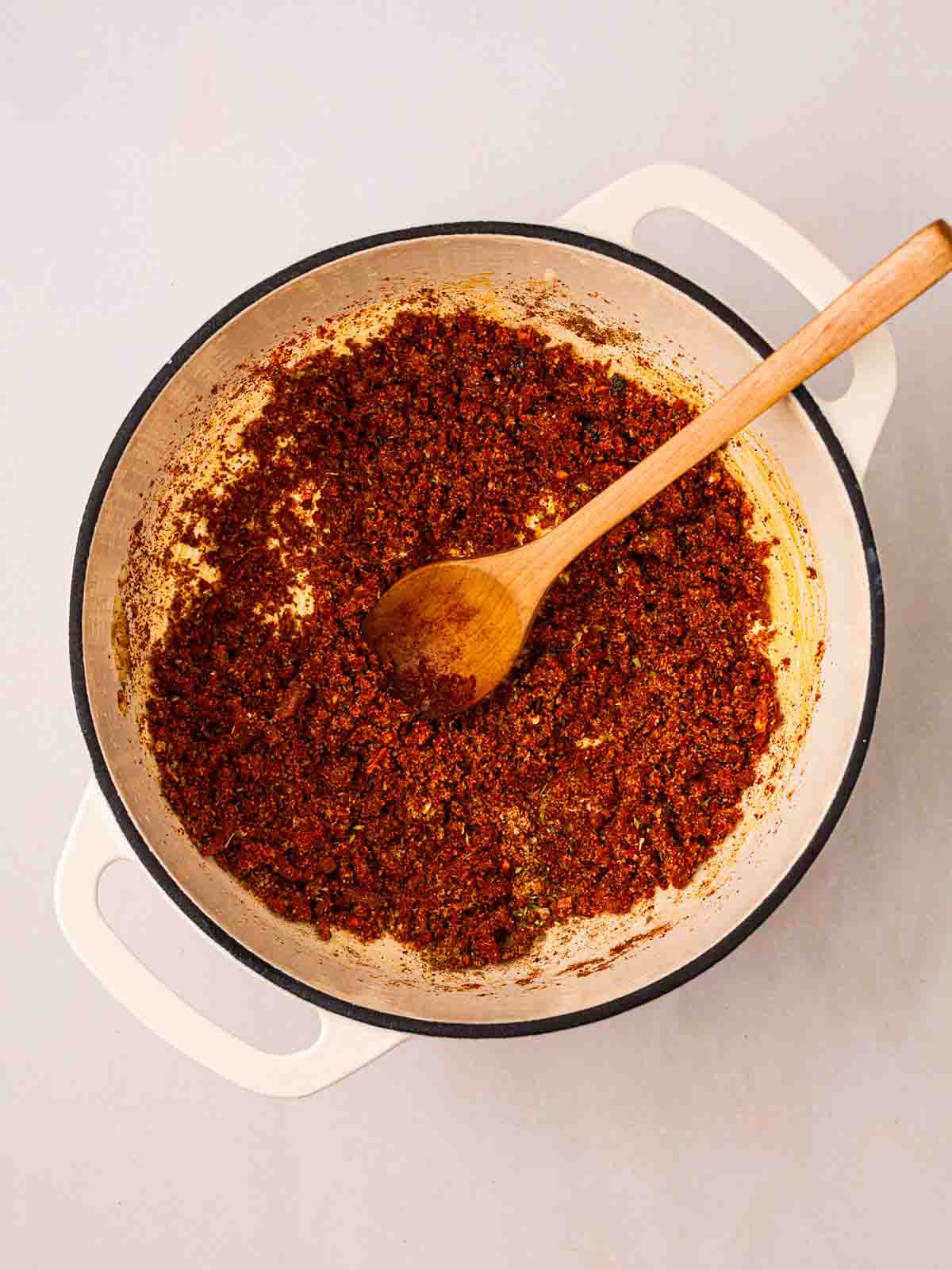 Spices cooking in a large pan with a wooden spoon.