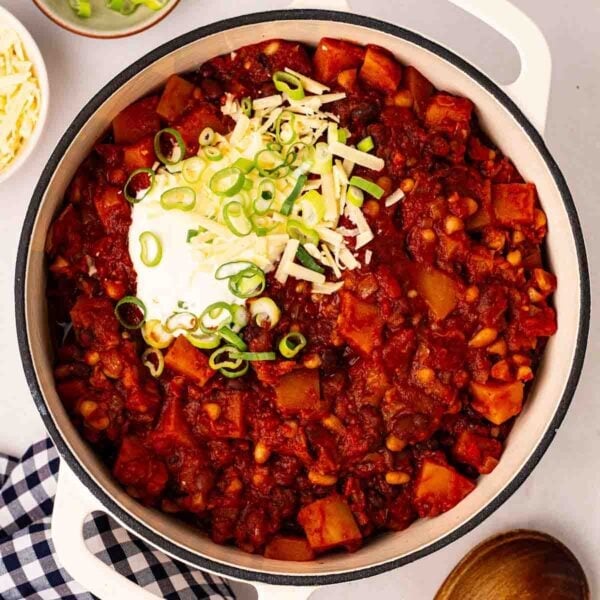 A pan filled with rich Veggie Chilli, with sour cream and spring onions on top.