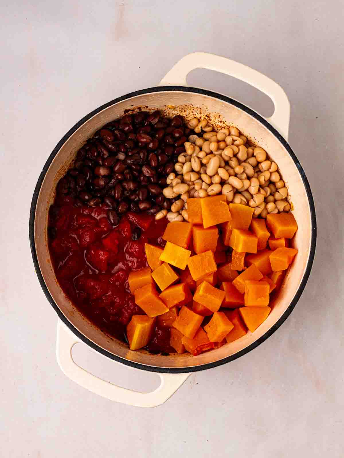 A pan filled with sweet potato, beans and tomatoes for step 2 in the process for Vegetarian Chilli.
