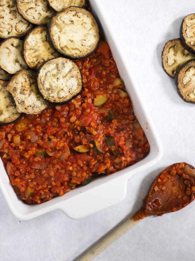 Aubergine slices on top of lentil rags in a white casserole dish. How to make Vegetarian Moussaka, step 4.