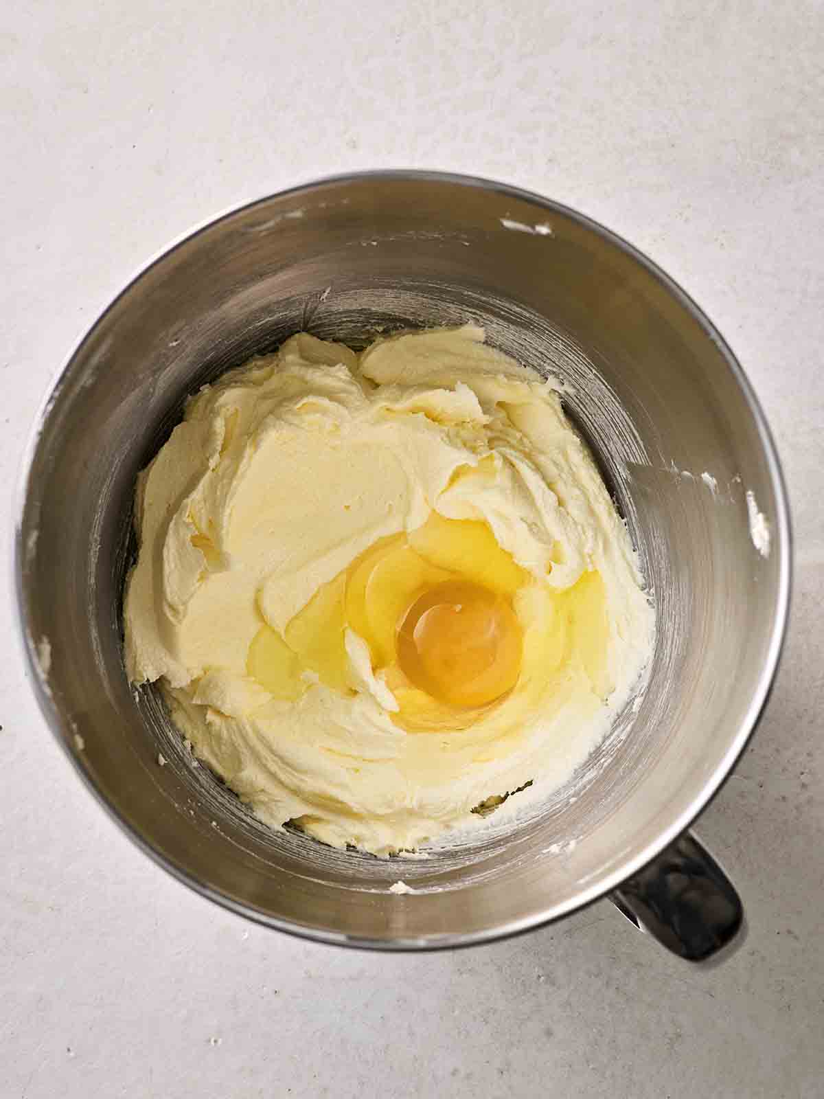A cake batter in a mixing bowl with an egg on top, ready to be mixed, for step 2 in the recipe for Victoria Sponge.