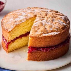 A Victoria Sponge Cake with a piece missing on a plate, ready to eat.