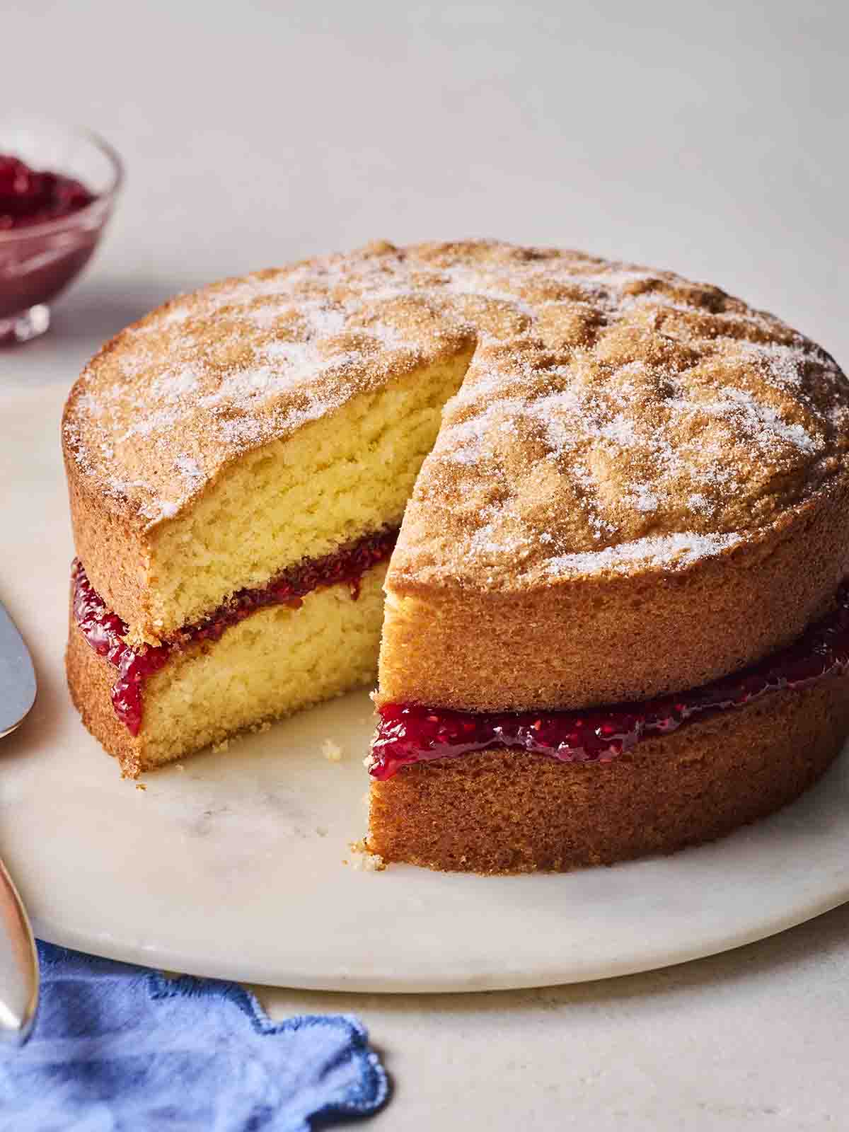A homemade Victoria Sponge Cake on a plate with a piece missing.